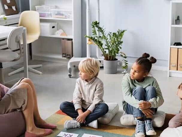 Patólogo del habla y lenguaje, SLP terapeuta del habla y lenguaje, fonoaudiólogo mostrando abecedario a niños pequeños sentados sobre cojines.