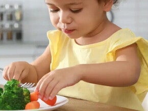 niña con camiseta amarilla comiendo un plato con verduras