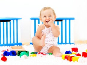 Bebé sonriendo sentado al lado de sus juguetes