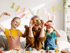 Padres y niños celebrando Pascua, cubriendo sus ojos con huevos de colores de forma divertida.