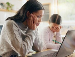 Madre y niña sentadas en la mesa de la cocina con una computadora portátil, realizando una actividad escolar en casa.