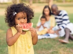 Niña comiendo sandía con su familia en el fondo