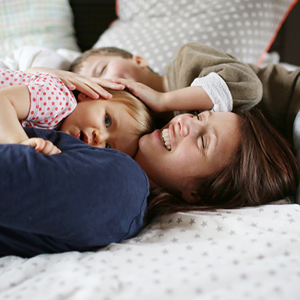 Estrategias efectivas para fomentar la autoestima de tus hijos Una mujer y dos niños felices acostados en una cama.
