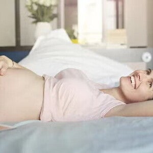 Mujer embarazada acostada sobre la cama, feliz, acariciando su vientre.