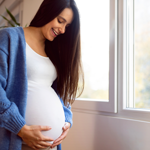 Consejos para un embarazo saludable Mujer embarazada vestida de blanco, sonriendo y sosteniendo su vientre con las manos.