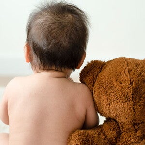 Pañalitis: ¿cómo prevenirla en los bebés? Bebé con pañal de espalda junto a un oso de peluche