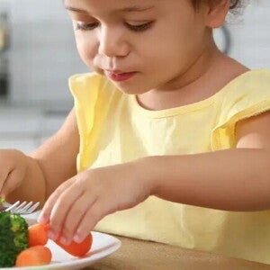 niña con camiseta amarilla comiendo un plato con verduras