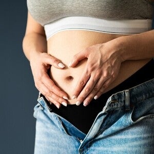 Abdomen de mujer embarazada en primer o segundo trimestre, manos en forma de corazón sobre el vientre.