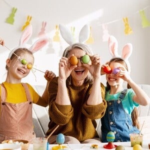 Padres y niños celebrando Pascua, cubriendo sus ojos con huevos de colores de forma divertida.