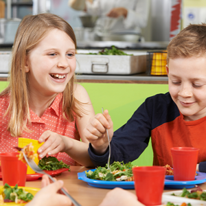 Alimentación saludable para niños escolares Niños comiendo en una cafetería escolar con platos de ensalada y pasta.