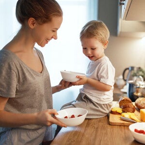 Madre y niño en la cocina, sentado en la mesada con un tazón, queso y pan, alimento energético