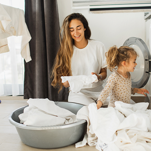 Fomentar la responsabilidad en los niños Madre e hija al lado de un lavarropas, con ropa blanca alrededor para fomentar responsabilidad en los niños.