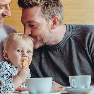 Conoce cuándo puedes darle galletas para bebés a tu hijo. Niña comiendo galletas para bebés con su papá y abuelo.