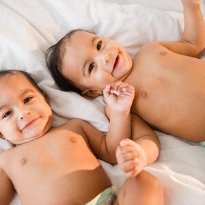 Identifica cuál es la diferencia entre los gemelos y los mellizos. Bebés gemelos sonriendo acostados en la cama.