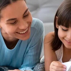 Por qué leer cuentos infantiles contribuye al desarrollo de los niños Madre ayuda a leer a su hija sonriendo