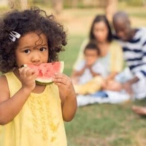 Niña comiendo sandía con su familia en el fondo