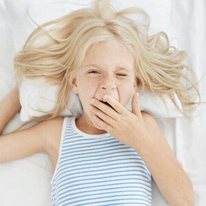 Niña rubia bostezando en la cama con ganas de dormir bien