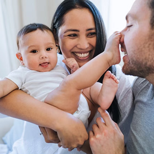 ¿Criar en equipo? Sí, se puede: descubre los beneficios de la crianza compartidaBeneficios de la crianza compartida Mamá carga al bebé sonriendo. Bebé tiene el pie en la nariz del papá.