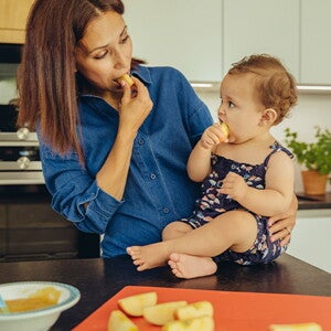Identifica cuáles son las frutas ideales para iniciar esta nueva etapa de tu bebé Mamá y bebé comiendo fruta en la cocina