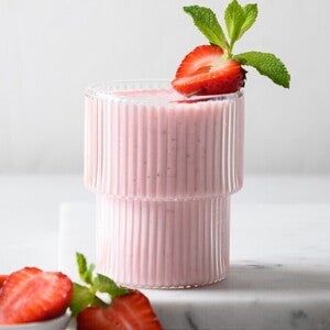 Batido Cremoso de Fresas Un vaso contiene batido de fresa y la fruta de decoración