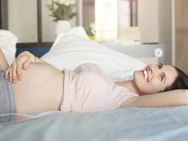 Mujer embarazada acostada sobre la cama, feliz, acariciando su vientre.