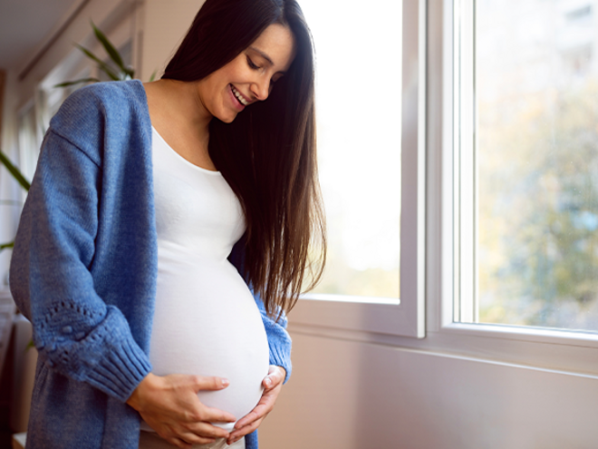 Consejos para un embarazo saludable Mujer embarazada vestida de blanco, sonriendo y sosteniendo su vientre con las manos.