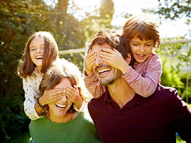 Hijos seguros y confiados Familia de cuatro disfrutando de un día soleado al aire libre. Dos adultos llevan a dos niños sobre sus hombros, rodeados de árboles y vegetación