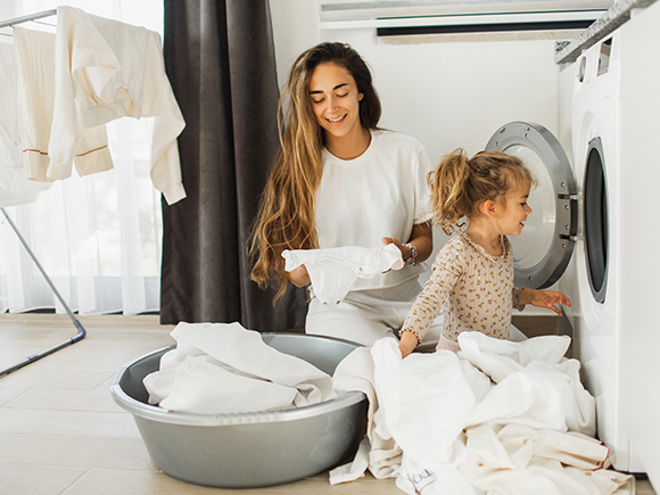 Fomentar la responsabilidad en los niños Madre e hija al lado de un lavarropas, con ropa blanca alrededor para fomentar responsabilidad en los niños.