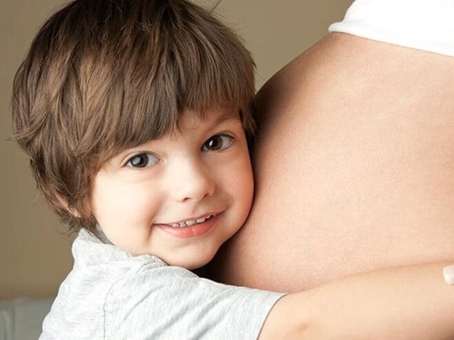 ¿Cómo decirle a mi hijo que tendrá un hermanito? Niño pequeño sonriendo y abrazando el vientre de mamá embarazada.