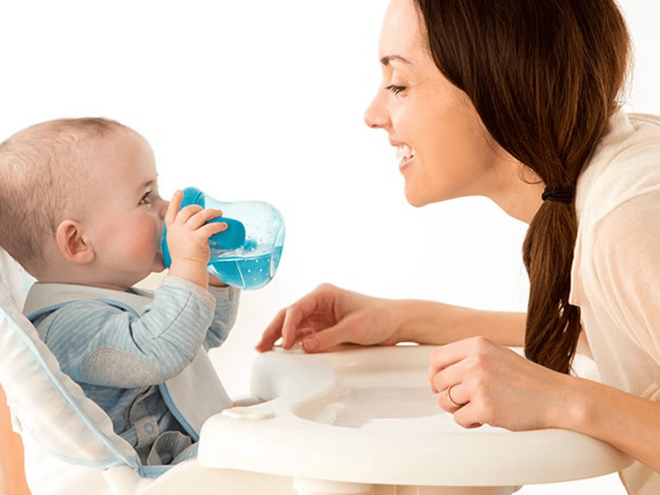 Cuándo dar agua al bebé Mujer adulta y bebé tomando agua en un vaso entrenador.