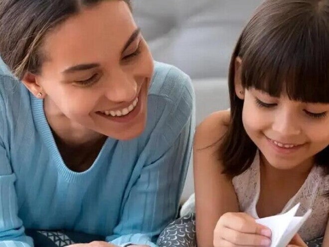 Por qué leer cuentos infantiles contribuye al desarrollo de los niños Madre ayuda a leer a su hija sonriendo