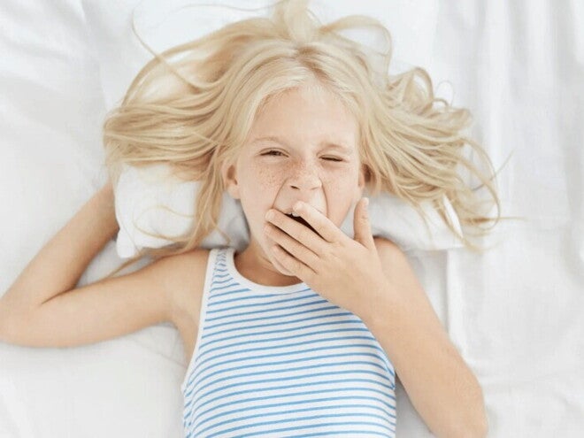 Importancia del sueño en los niños y su desarrollo Niña rubia bostezando en la cama con ganas de dormir bien