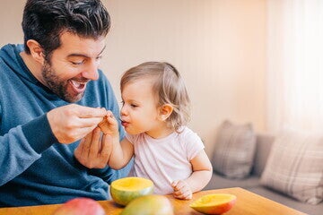 Un padre sonriendo mientras da de comer papilla a su bebé Un padre sonriendo mientras da de comer papilla a su bebé