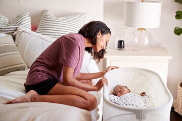 Una madre sentada al lado de la mecedera con su bebé dentro Una madre sentada al lado de la mecedera con su bebé dentro