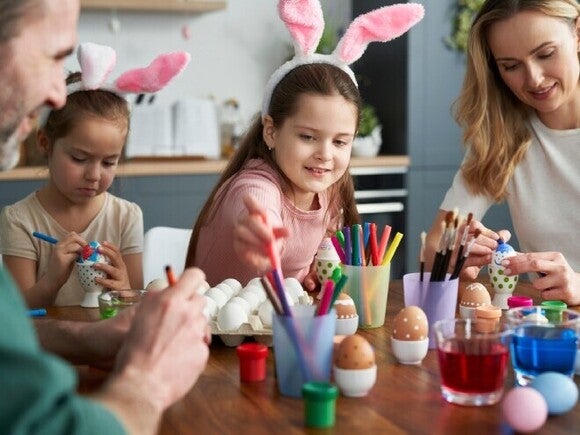 Familia caucásica feliz de cuatro personas decorando huevos de Pascua en casa.