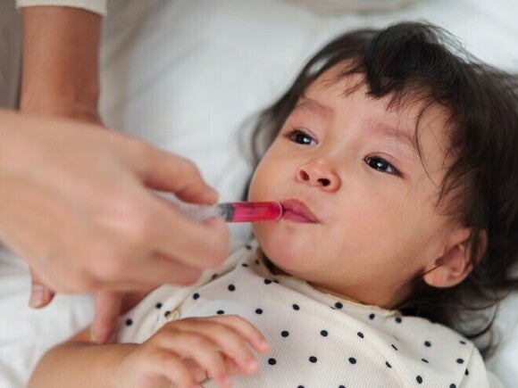 Persona adulta administrando medicamento líquido a un niño pequeño con una jeringa dosificadora.