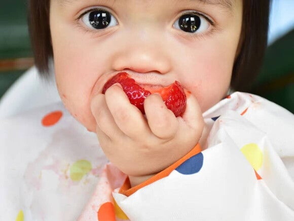 Beneficios del BLW Niña pequeña comiendo fresa con las manos.