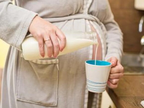 Mujer embarazada, sirviendo una taza con leche, calcio para embarazo.