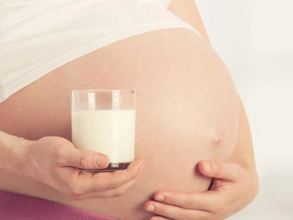 Mujer embarazada, sosteniendo su vientre y un vaso de leche, calcio para embarazo.