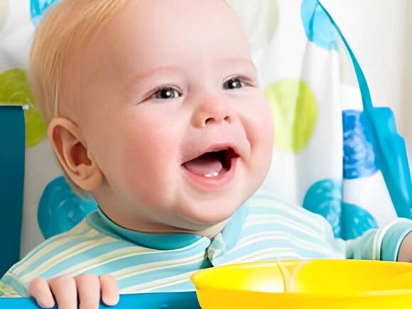 Bebé en silla alta sonriendo con un plato de alimentos sólidos frente a él.