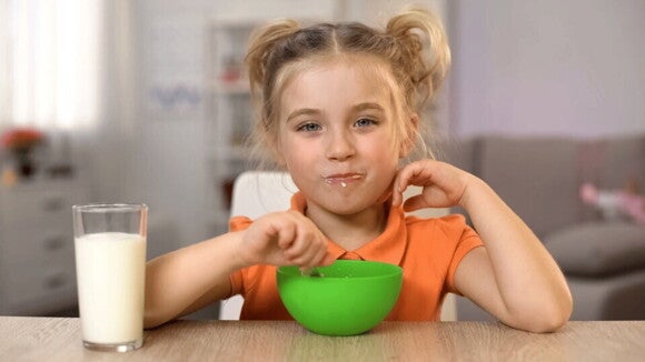 Es fundamental que desarrolle el sentido de saciedad niña sonriendo mientras desayuna