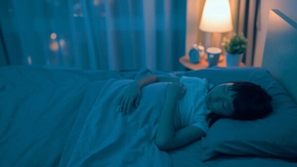 Beneficios de dormir bien para los niños Niña que tiene buenos hábitos de sueño duerme tranquila en su cuarto con una lámpara prendida de fondo