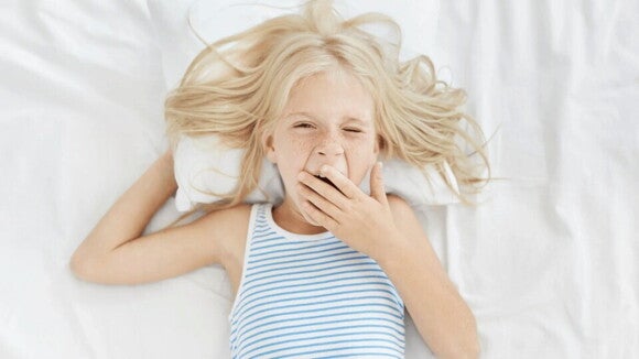 Hábitos saludables para niños con respecto al buen sueño Niña rubia bostezando en la cama con ganas de dormir bien