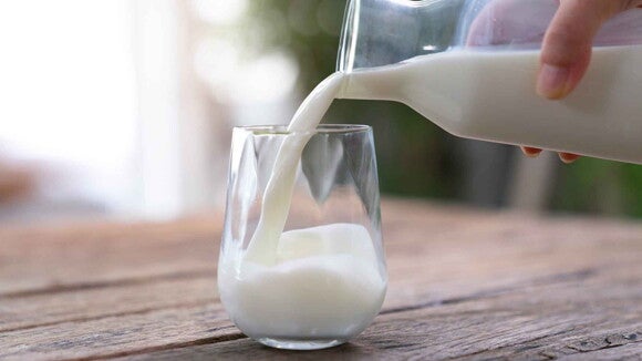 Una persona sirviendo un vaso de leche deslactosada en polvo