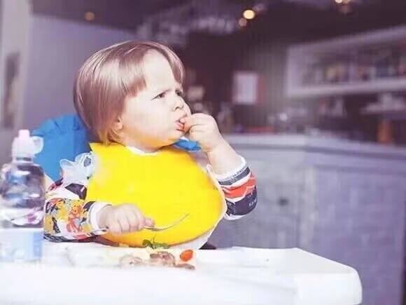 Reglas básicas para implementar el Baby-Led Weaning Niño pequeño en una silla alta, con babero, y alimentándose con las manos.