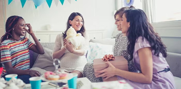 Futura mamá rodeada de amigas y abriendo regalos en fiesta de revelación de género del bebé.