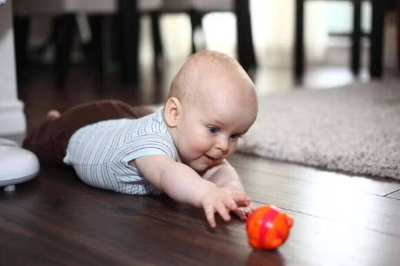 Bebé de 7 meses haciendo tummy time, acostado boca abajo, intentando alcanzar un juguete con la mano.