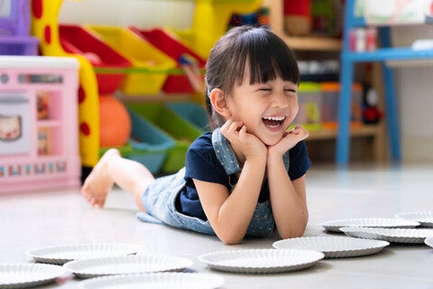 Niña acostada en un cuarto de juegos, riendo. Concepto de comportamiento, emociones y desarrollo emocional en niños.